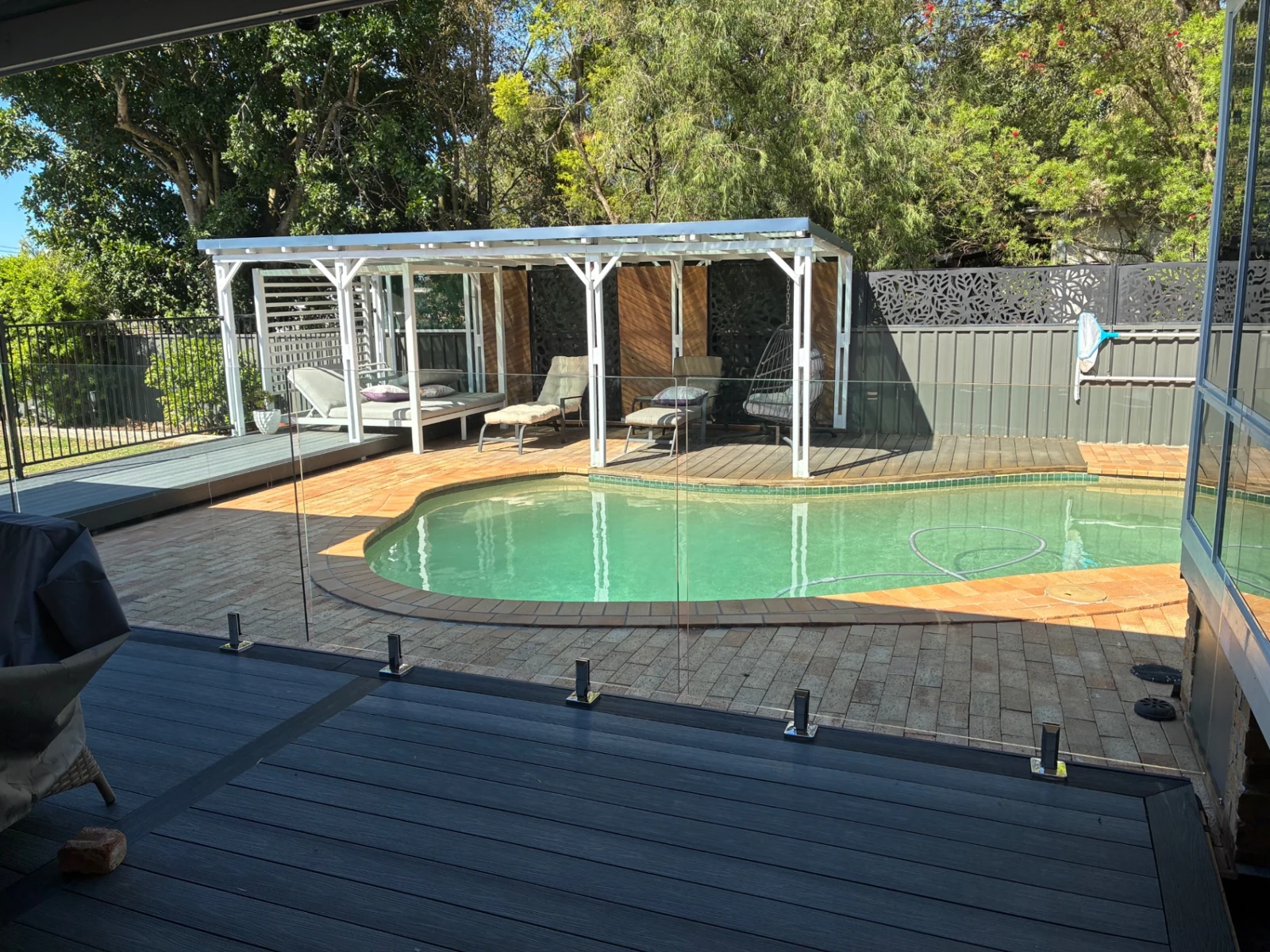 Glass pool fencing viewed from a deck beside a swimming pool and covered outdoor area