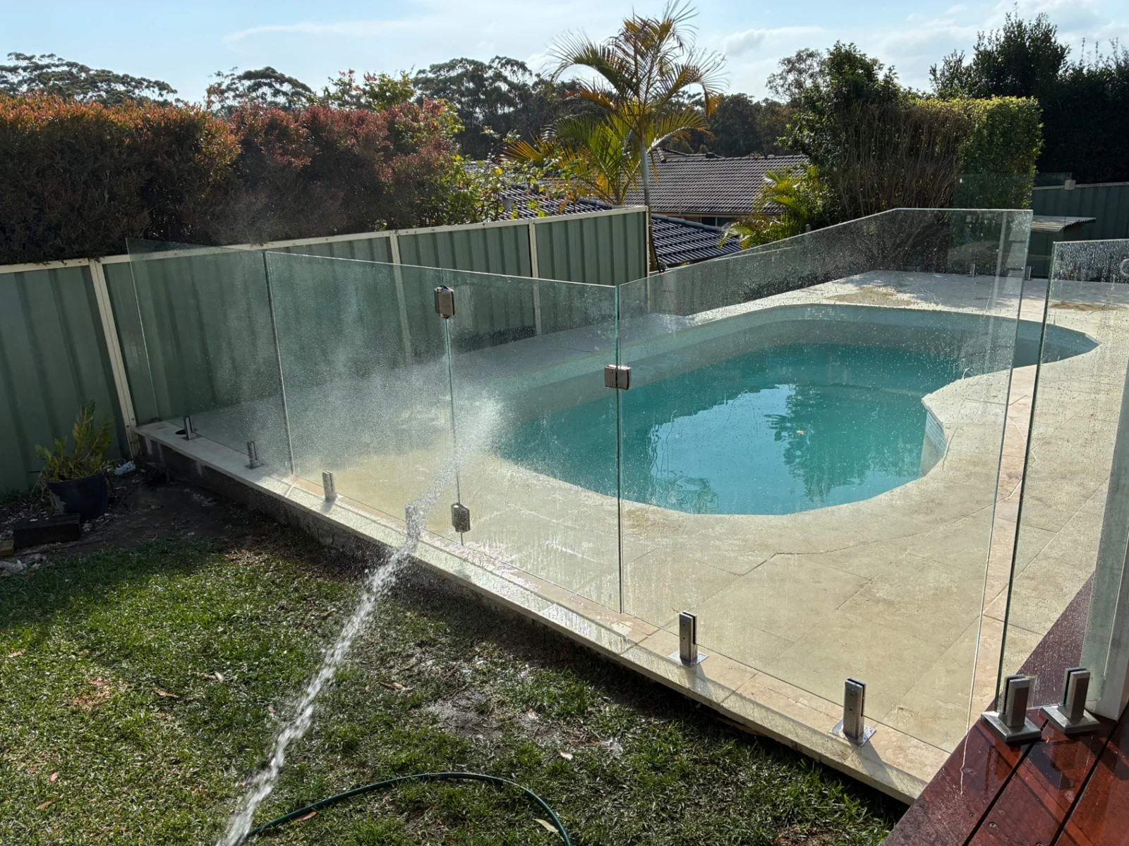 Clear glass pool fence with stainless-steel fittings around a curved swimming pool