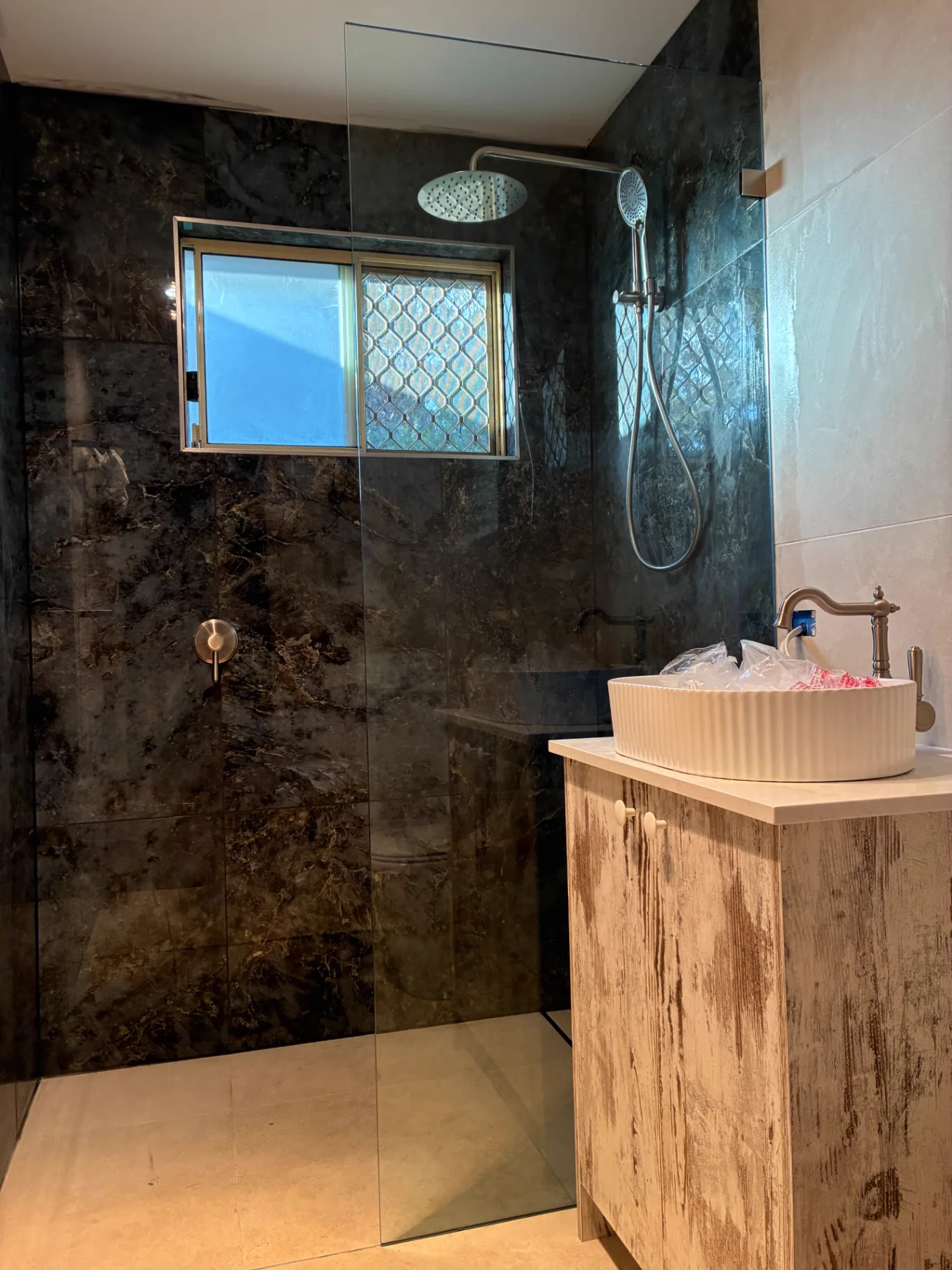 Custom fixed walk-in glass shower panel beside dark marble tiles installed by Pinnacle Glass & Timber