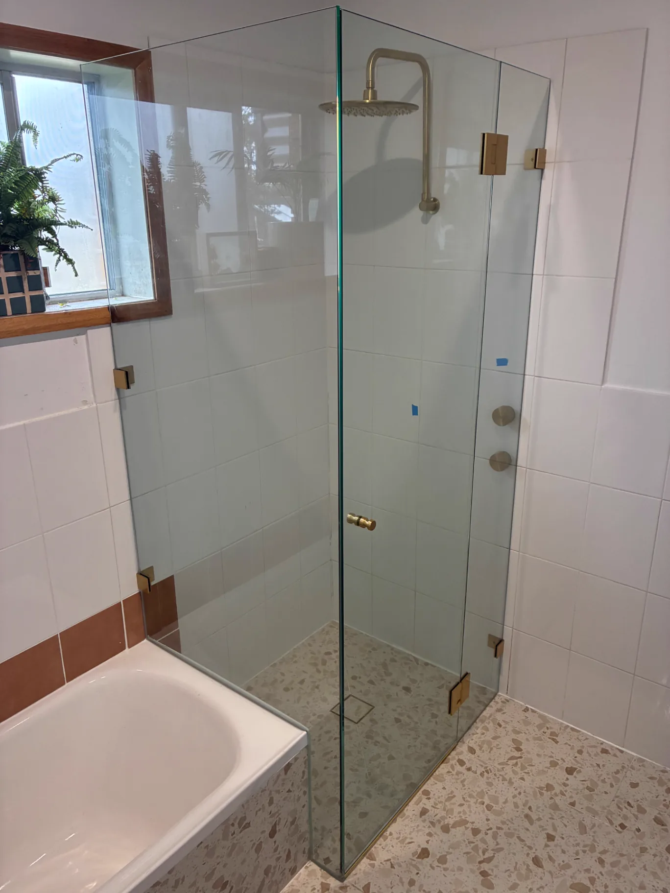 Custom frameless glass shower screen with brushed-gold hardware installed by Pinnacle Glass & Timber